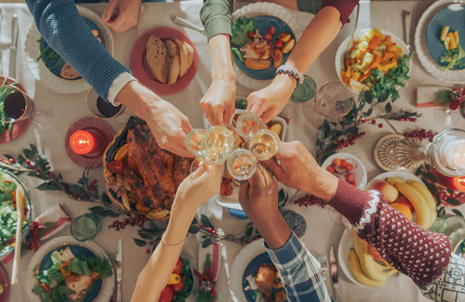 Vedere de sus a unei mese de iarnă festive, la care mai multe persoane ciocnesc pahare.